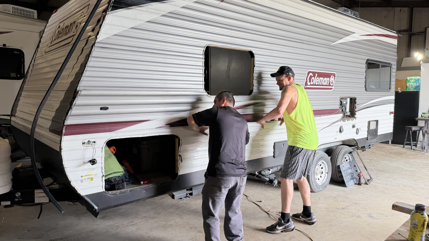 Two technicians fitting a sidewall panel on a travel trailer at the RepairAnyRV shop in Princeton, TX